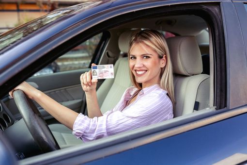 Γυναίκα σε αυτοκίνητο που κρατά ψηλά μια άδεια οδήγησης, χαμογελώντας.