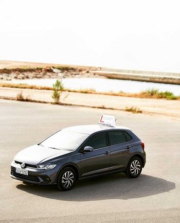 Γκρι VW Polo που οδηγεί σε ασφαλτοστρωμένη επιφάνεια, με πινακίδα στην οροφή που λέει 