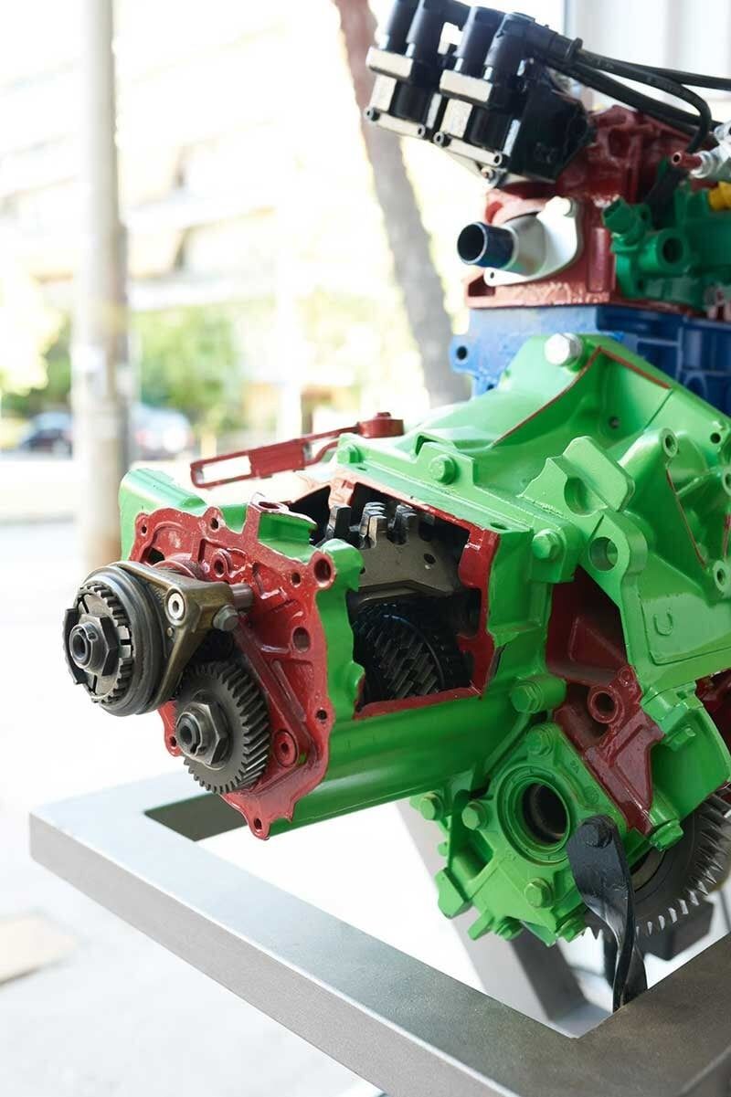 Τομή ενός πράσινου και κόκκινου κινητήρα, που αποκαλύπτει γρανάζια και εσωτερικά εξαρτήματα σε μεταλλική βάση.