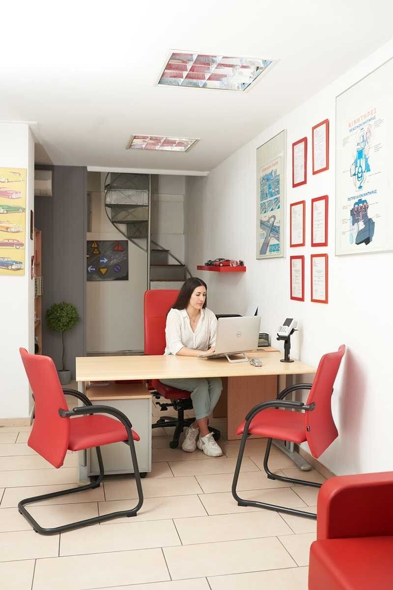 Γυναίκα σε ένα γραφείο με κόκκινες καρέκλες, χρησιμοποιώντας ένα φορητό υπολογιστή.