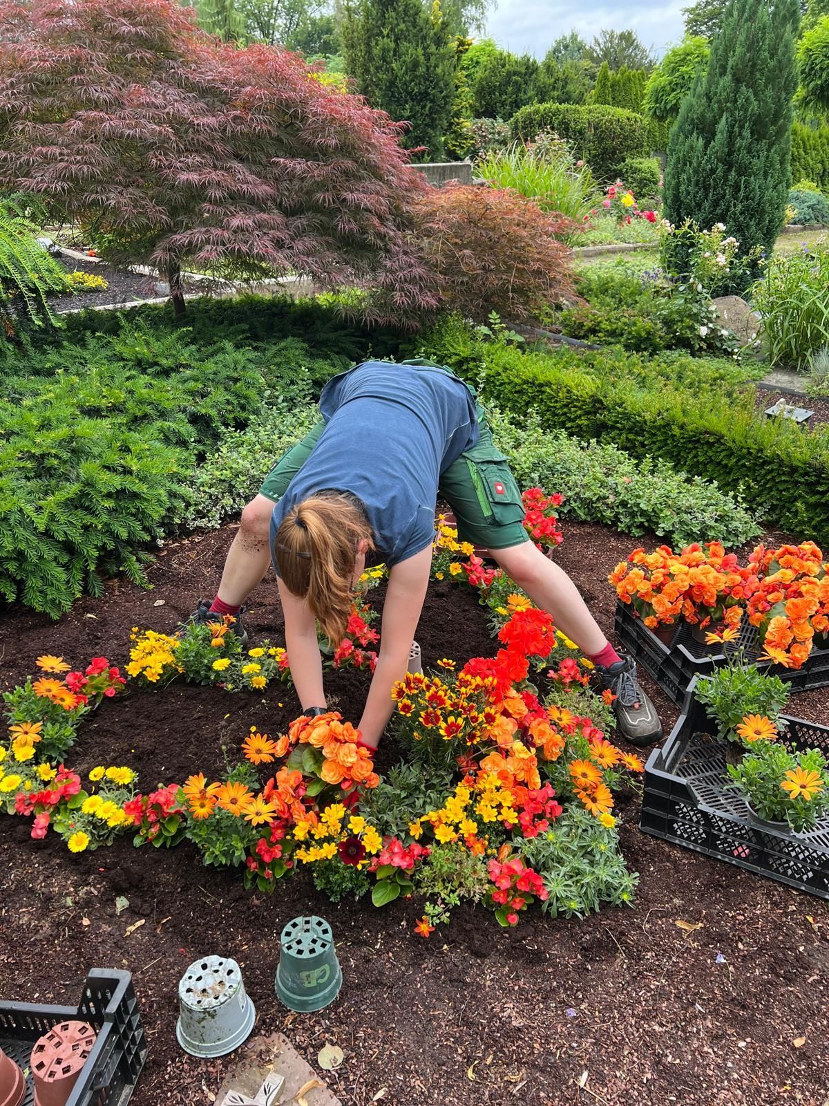 Eine Frau bückt sich, um in einem Garten Blumen zu pflanzen.