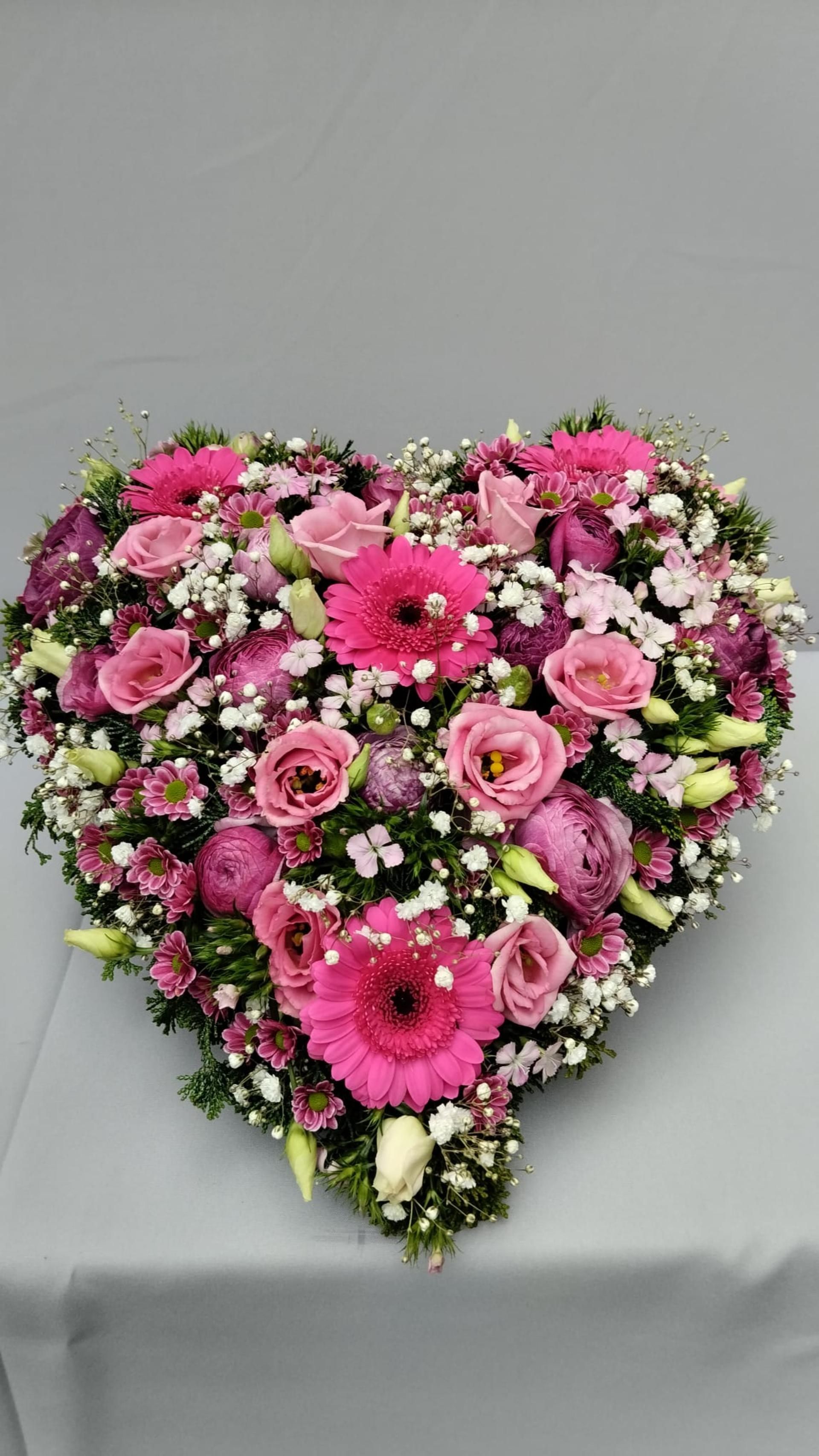 Auf einem Tisch steht ein herzförmiges Arrangement aus rosa Blumen.