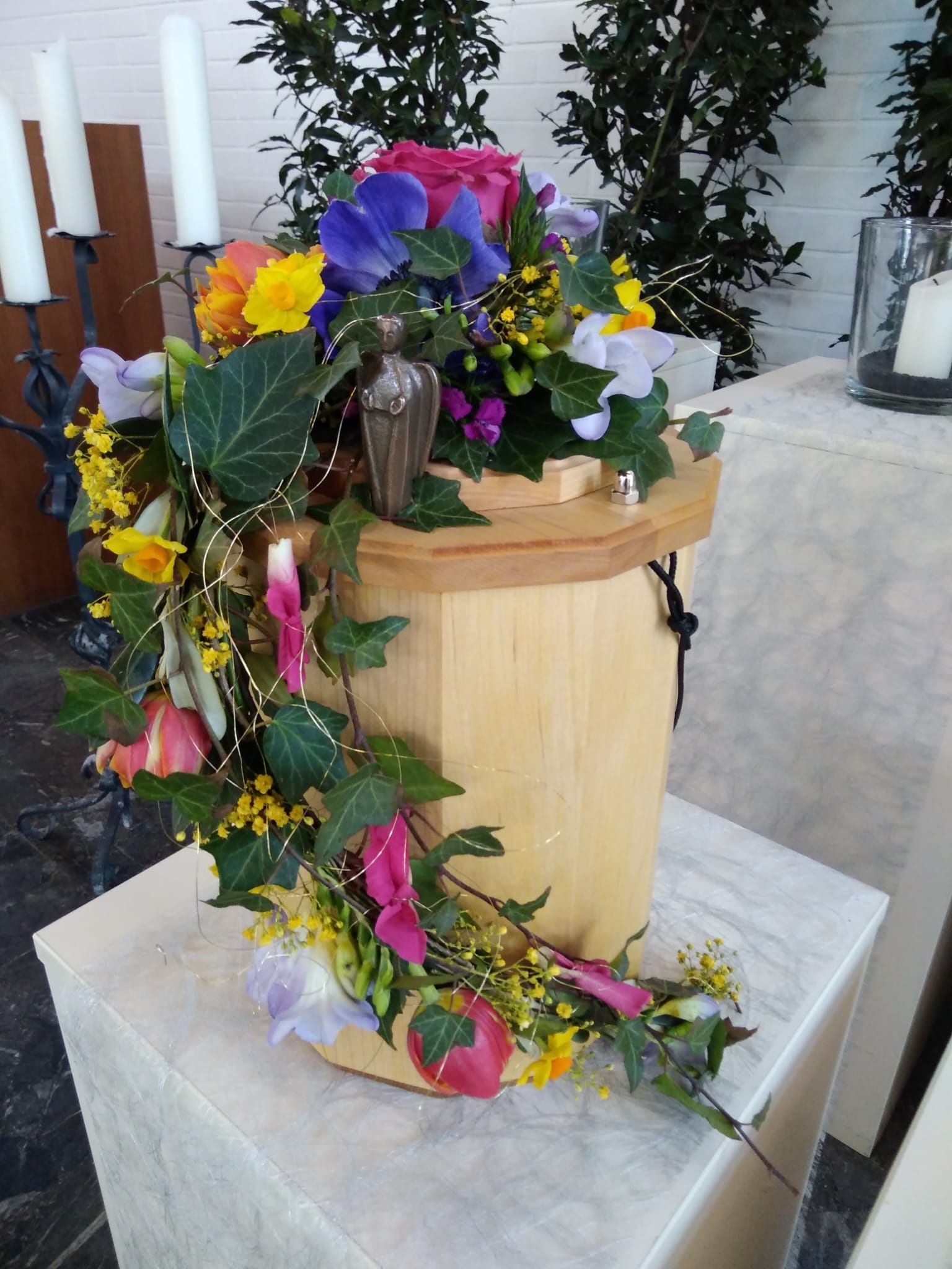 Auf einem Tisch steht eine mit Blumen gefüllte Holzurne.