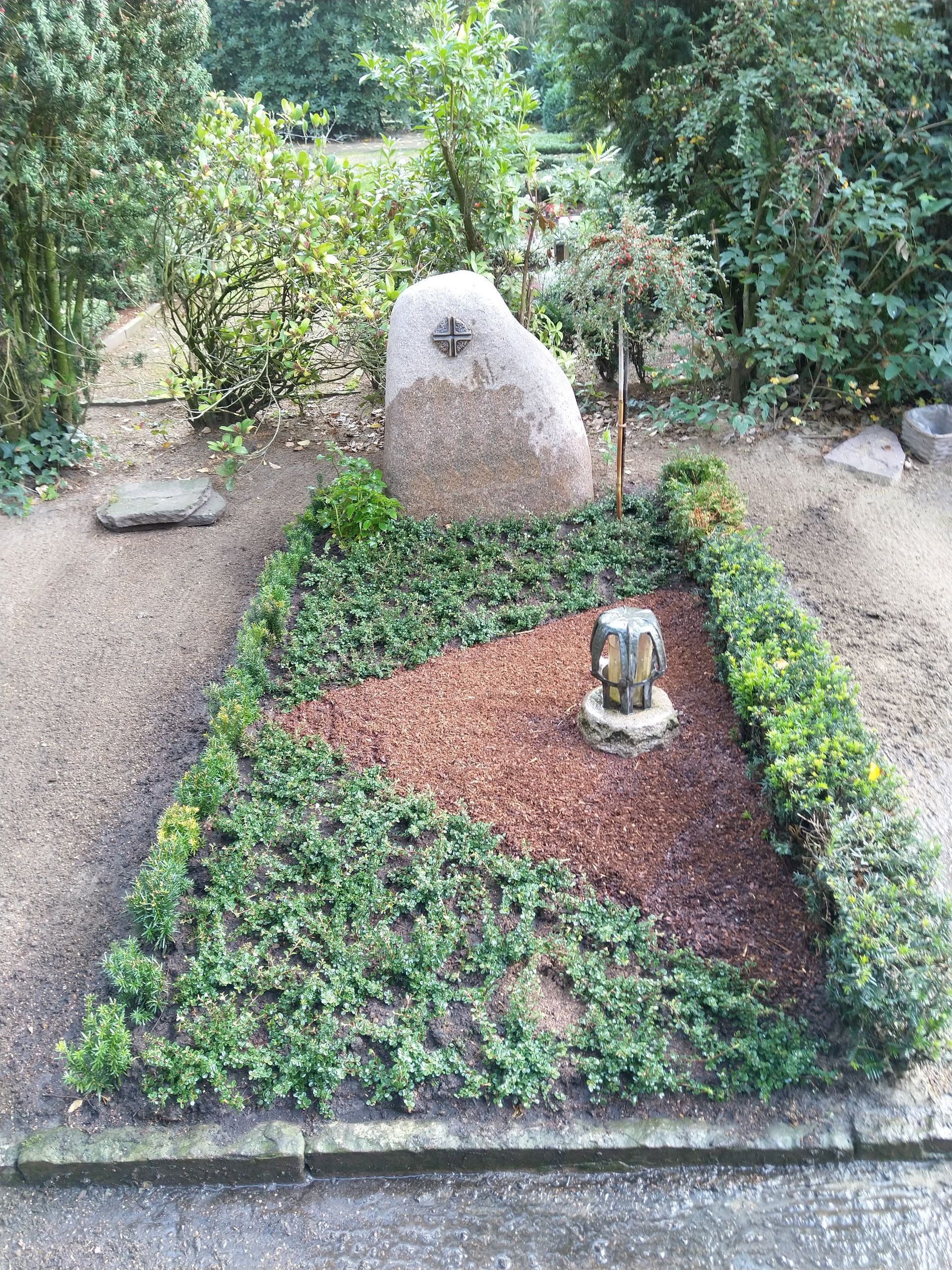 Ein Friedhof mit einem großen Felsen in der Mitte, umgeben von Pflanzen und Büschen.
