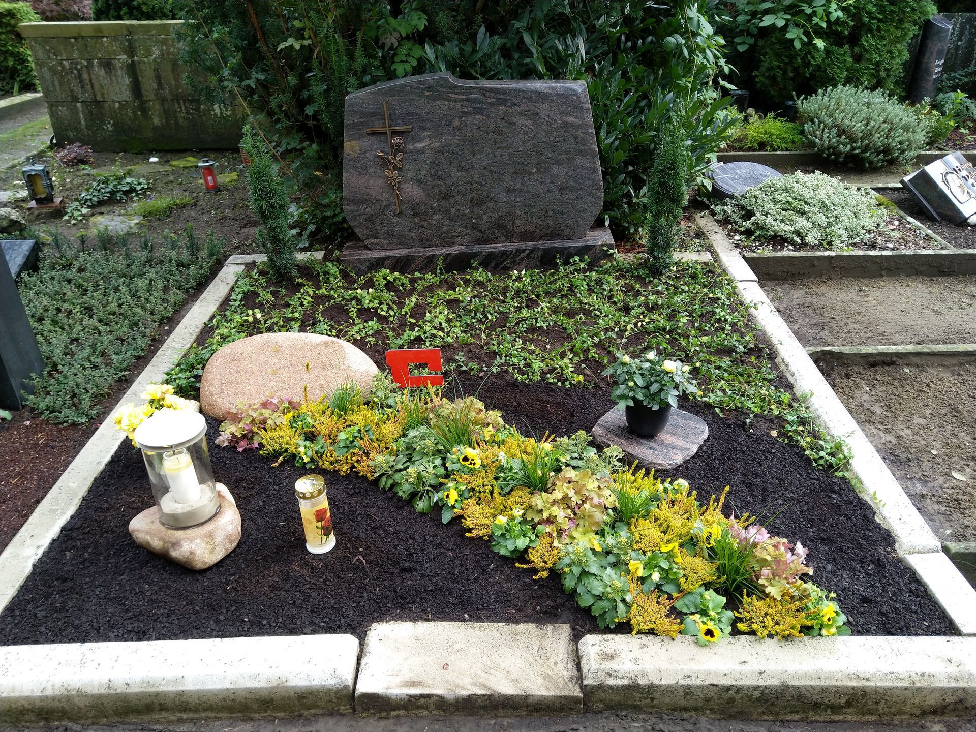 Ein Grab mit Blumen und einer Kerze darauf auf einem Friedhof.