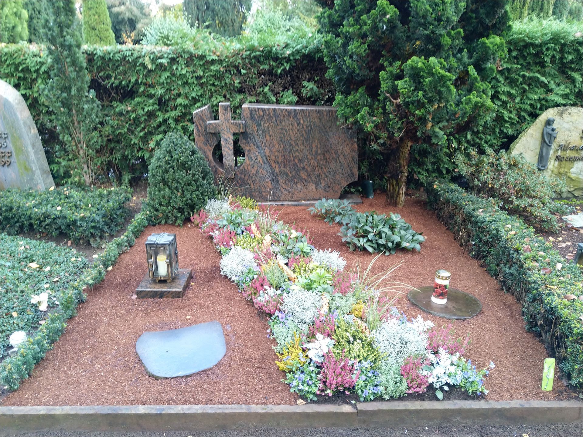 Ein Grab mit Blumen und einem Kreuz darauf auf einem Friedhof.