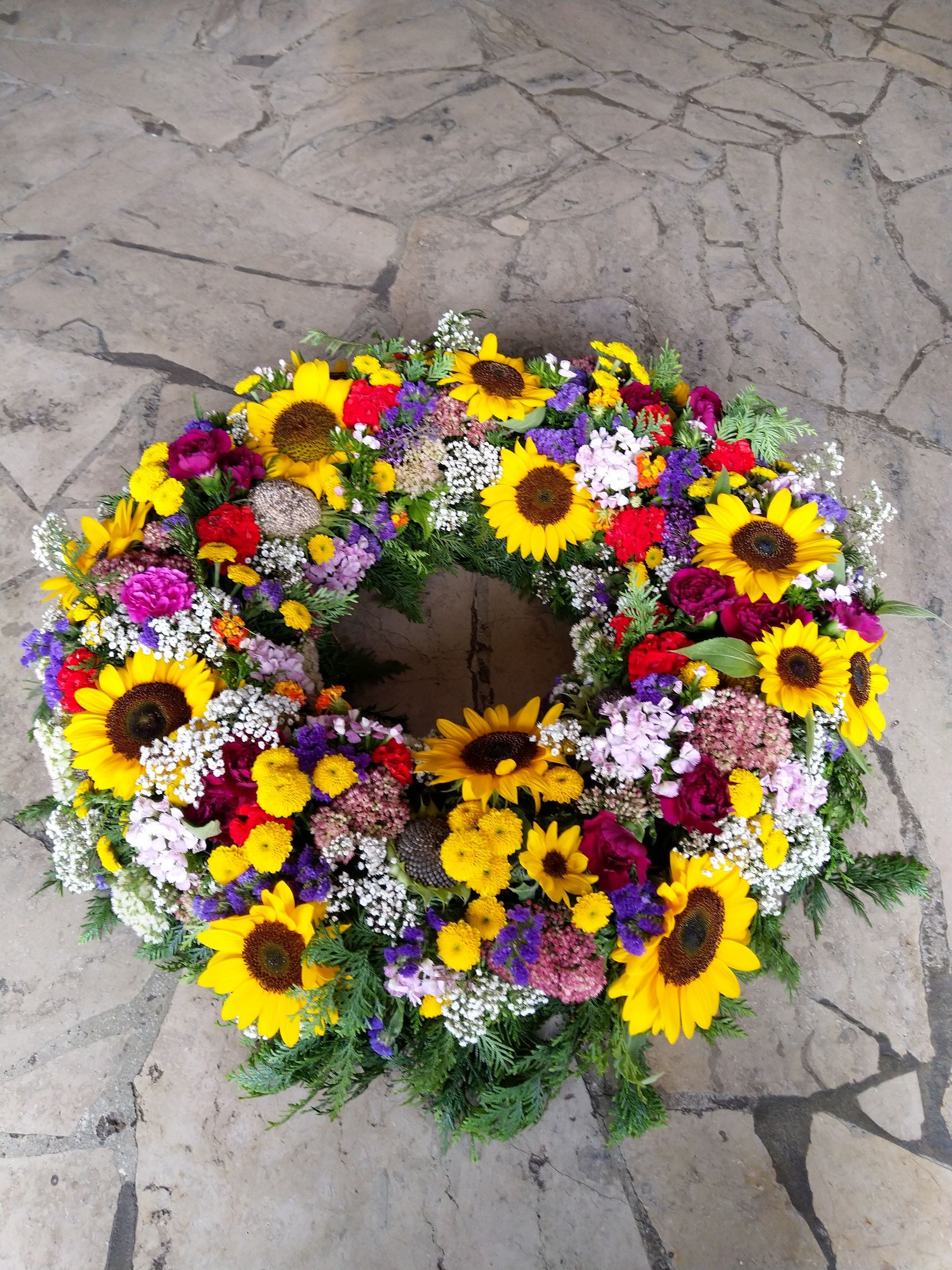 Ein Kranz aus Sonnenblumen und anderen Blumen auf einem Steinboden