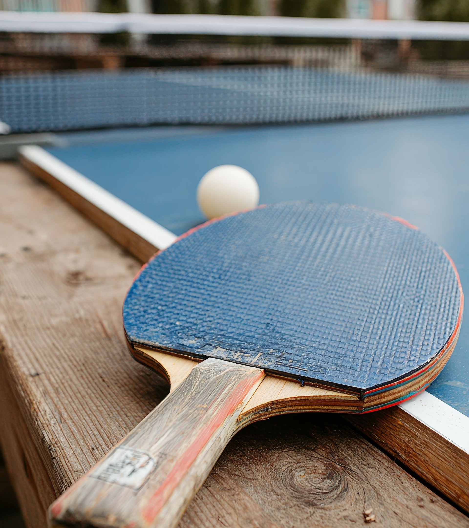 Raquette de ping-pong sur une table bleue avec une balle blanche et un filet.