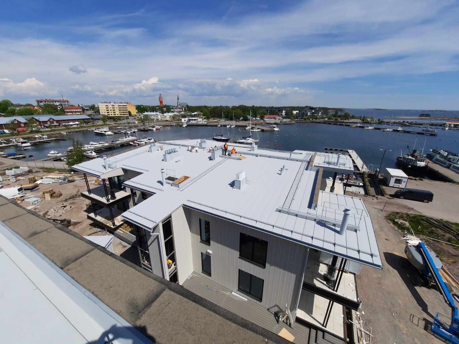 Rakennustyömaa rantanäköalalla; harmaa rakennus tasakatolla, satama, sininen taivas.