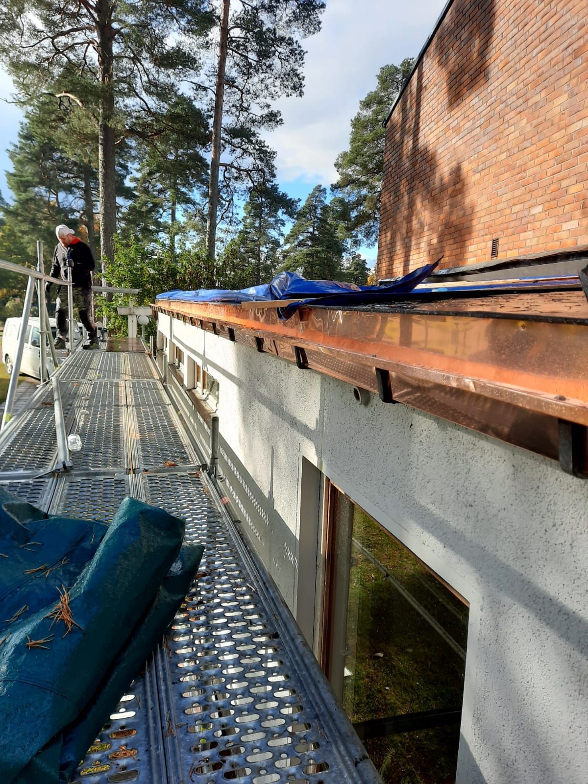 Henkilö rakennustelineillä lähellä rakennusta, jossa on näkyviä kattovaurioita ja roskia.
