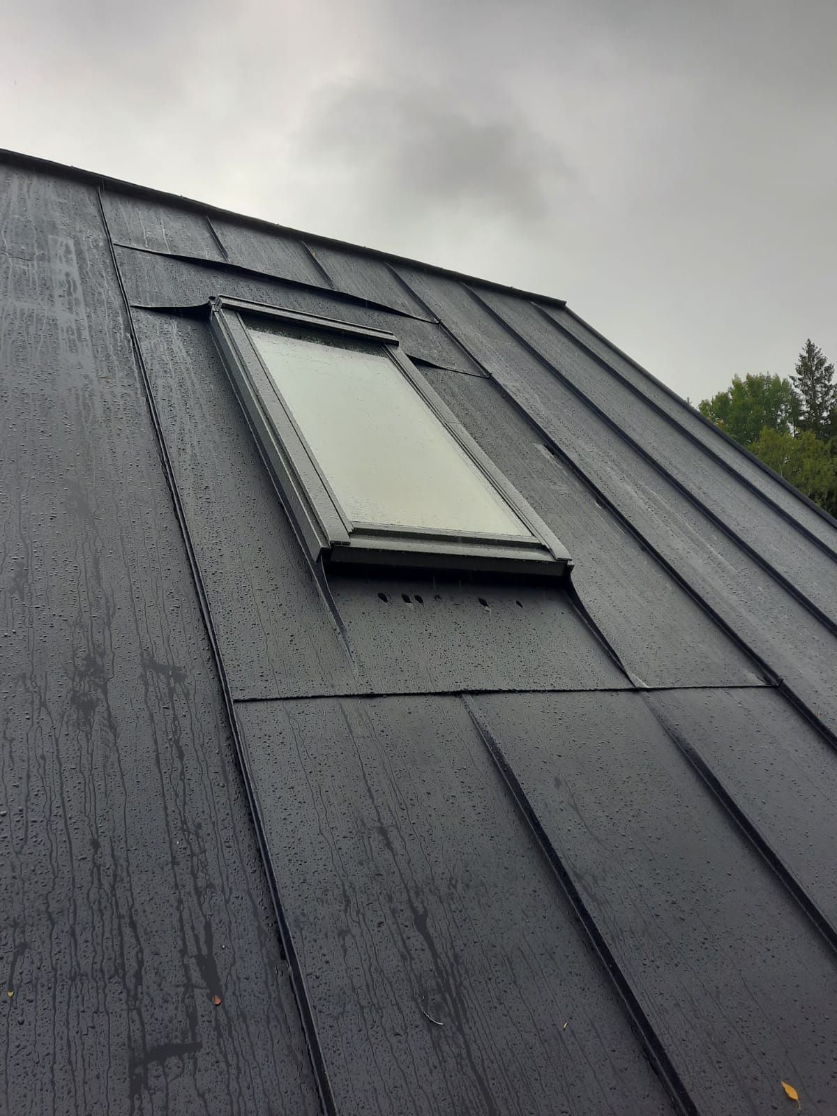Musta metallinen katto ja suorakaiteen muotoinen kattoikkuna pilvisenä päivänä.
