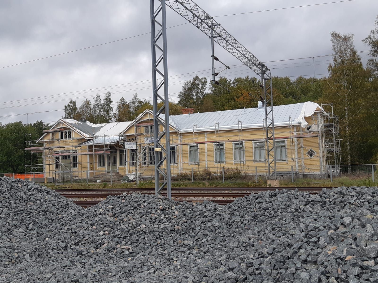Keltainen puurakennus remontissa lähellä rautatien ja soran seutua.