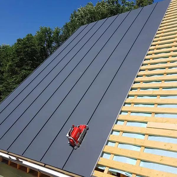 Harmaata peltikattoa asennetaan harjakatolle; punainen työkalu on käytössä.