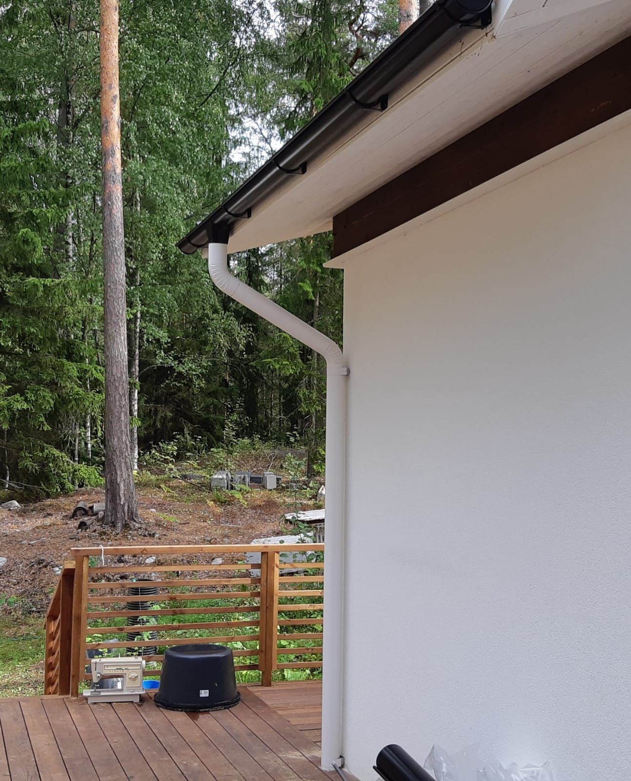 Valkoinen talon julkisivu mustilla ränneillä, puisen terassin ja puiden ympäröimänä.