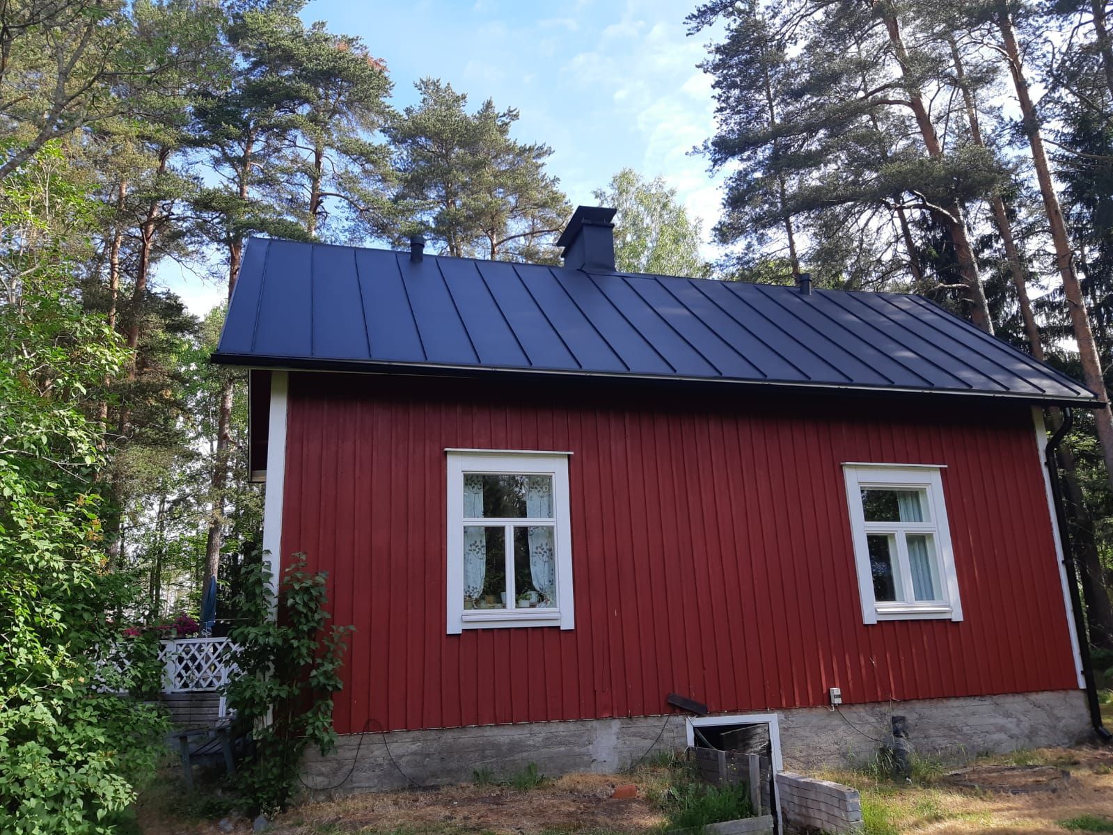 Punainen puutalo, jossa valkokehyksiset ikkunat, tumma katto ja savupiippu, puiden keskellä.