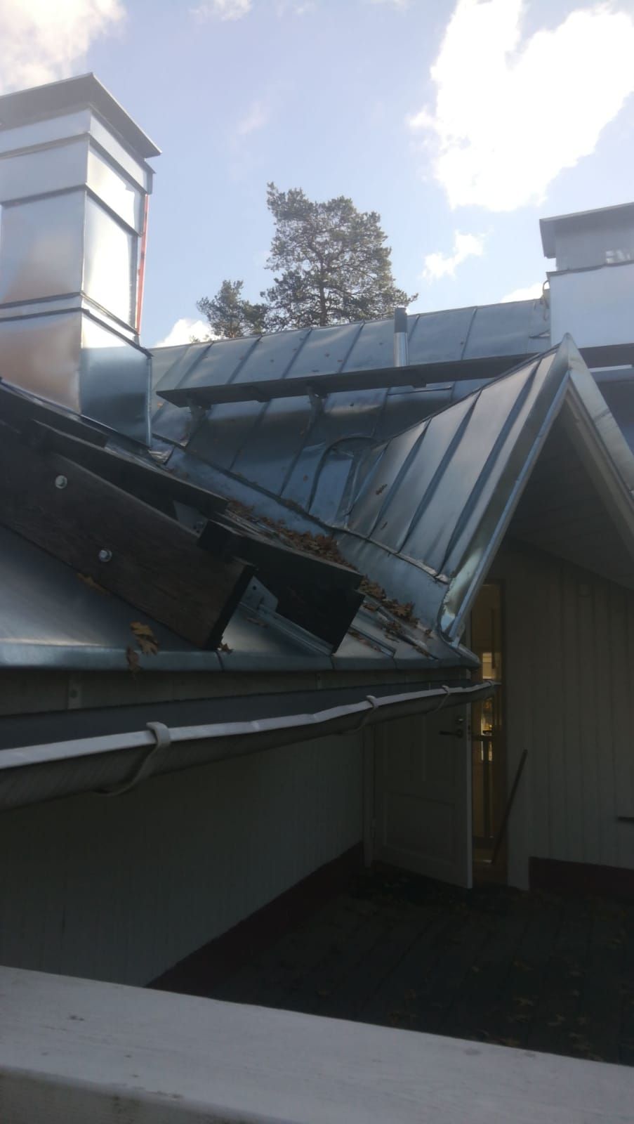 Rakennuksen metallikatto, jossa on kaksi savupiippua, osittain pilvistä taivasta vasten.