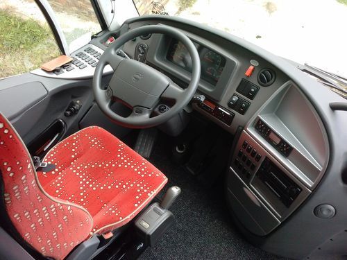 El interior de un autobús con asientos rojos y un volante.