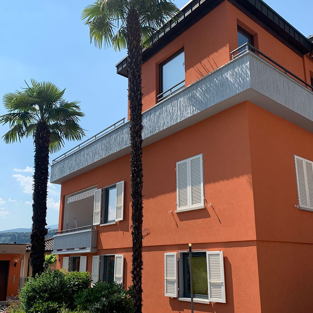 Edificio in stucco arancione con palme e persiane bianche.