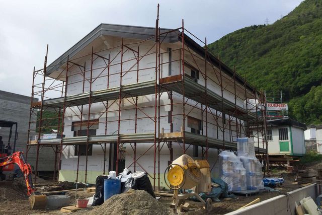 Edificio in costruzione, con impalcature, isolamento in schiuma e materiali da costruzione visibili.