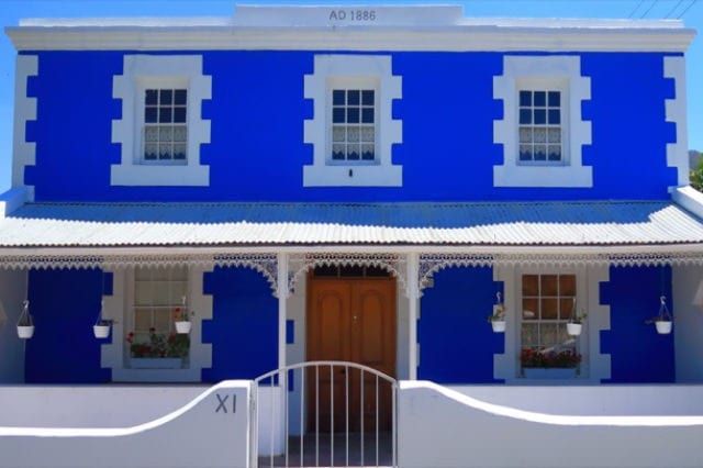 Casa storica blu e bianca con finiture decorative, tre finestre al piano superiore e due al piano inferiore.