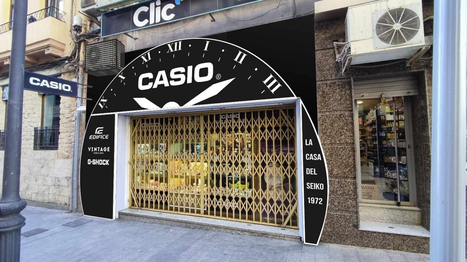 Un local comercial con un gran letrero de reloj CASIO arqueado sobre una verja metálica dorada, situado en una acera de la ciudad.
