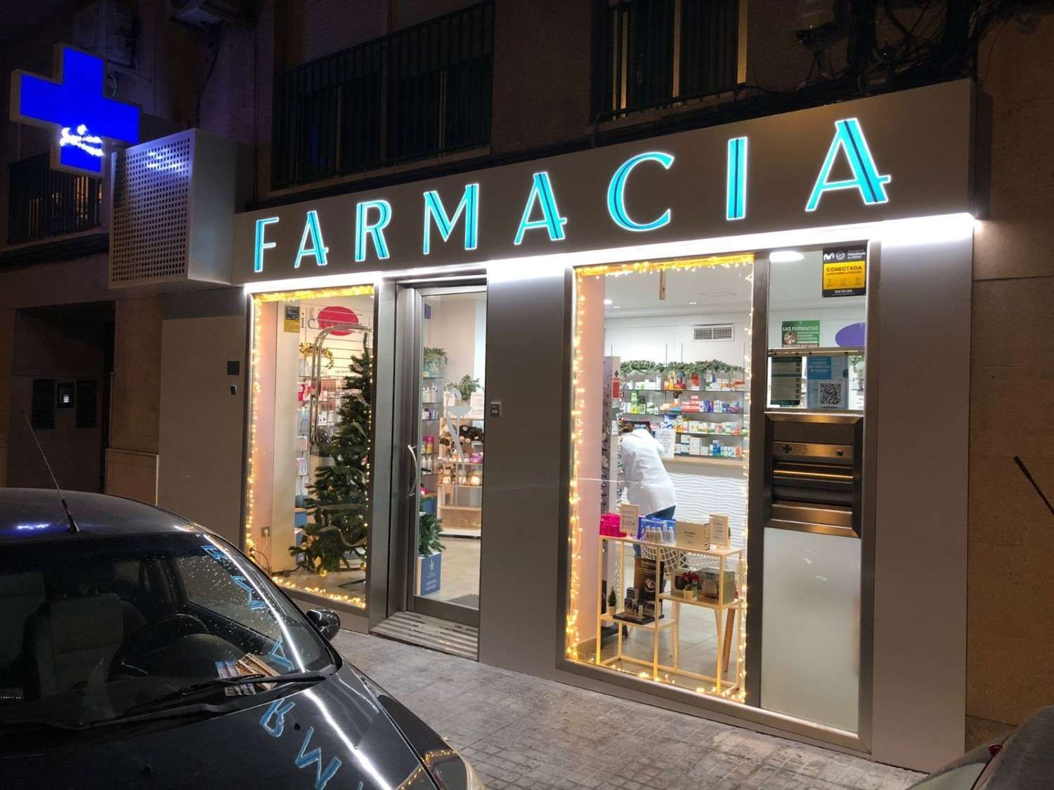 La fachada de una farmacia por la noche, con un letrero brillante e iluminado que dice 