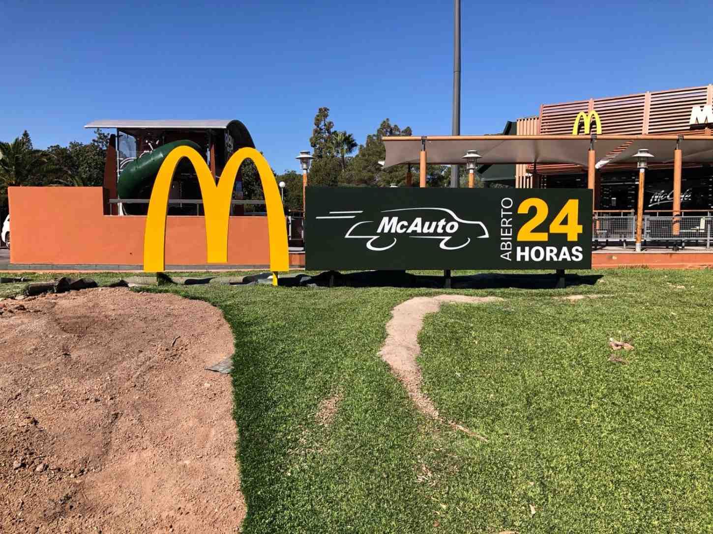 Un restaurante McDonald's con un letrero amarillo de los Arcos Dorados y un cartel negro que anuncia el servicio McAuto las 24 horas en el césped.