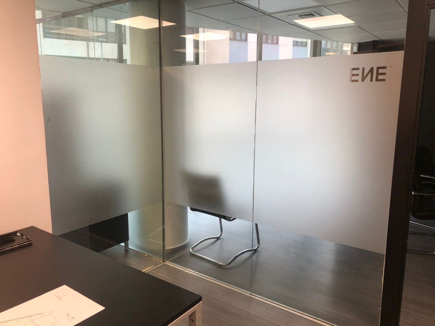 Un interior de oficina moderno con mamparas de vidrio con paneles esmerilados y el logotipo de ENE, visto desde un escritorio oscuro.