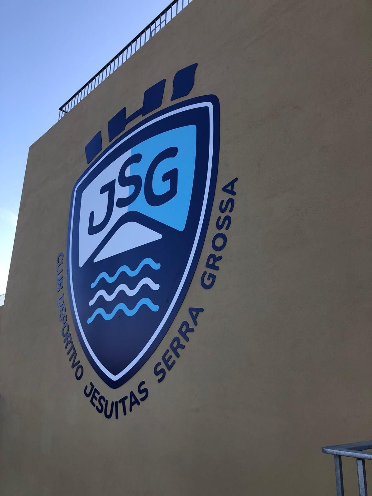 Un mural en una pared de color beige muestra el escudo azul marino y azul claro del Club Deportivo Jesuitas Serra Grossa.