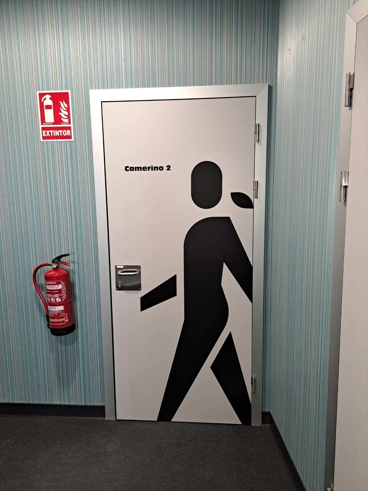 Una puerta blanca con un pictograma negro de una persona caminando, con la etiqueta 