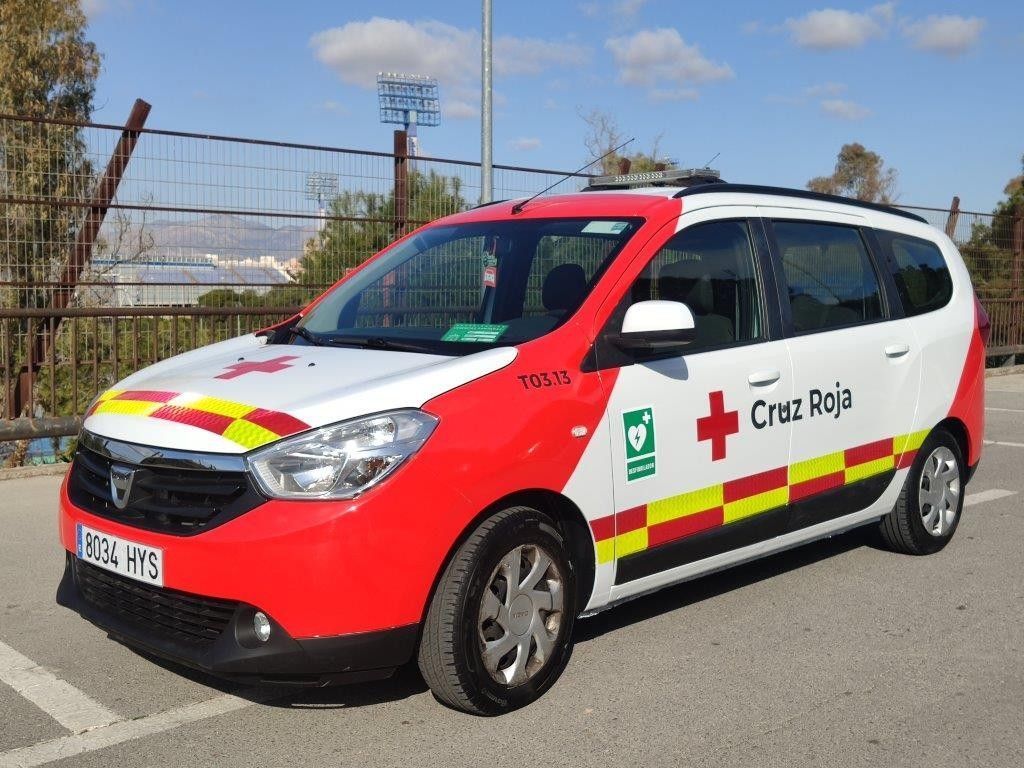 Un vehículo de emergencia Dacia de la Cruz Roja, de color blanco y rojo, estacionado al aire libre en un día soleado.