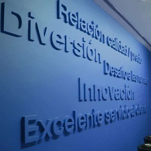 Una pared azul presenta letras blancas tridimensionales que muestran los valores corporativos en español, incluyendo 