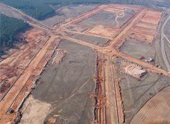 Vista aérea de una obra en construcción con caminos de tierra nivelados, desbroce para el desarrollo urbanístico y bosques circundantes.