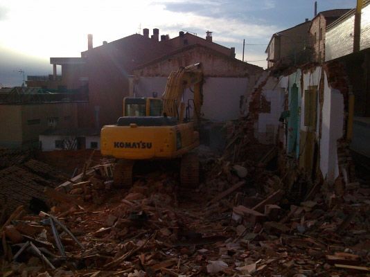 Una excavadora Komatsu amarilla demoliendo la estructura de un edificio en un solar lleno de escombros.