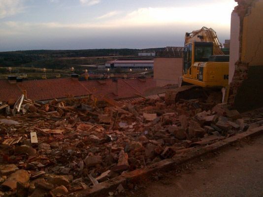 Una excavadora amarilla reposa sobre un montón de escombros en una obra de demolición al anochecer.
