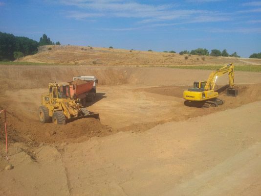 Maquinaria de construcción amarilla excava y transporta tierra en una gran obra al aire libre bajo un cielo azul despejado.