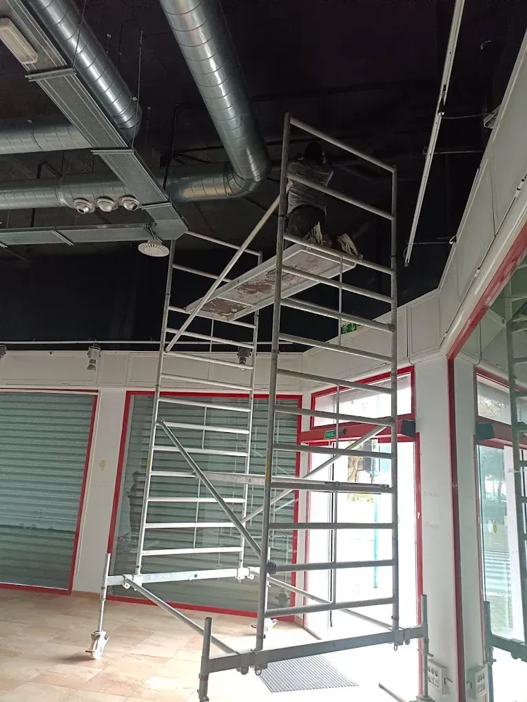 Andamios en el interior de un edificio con puertas enrollables y techo negro.