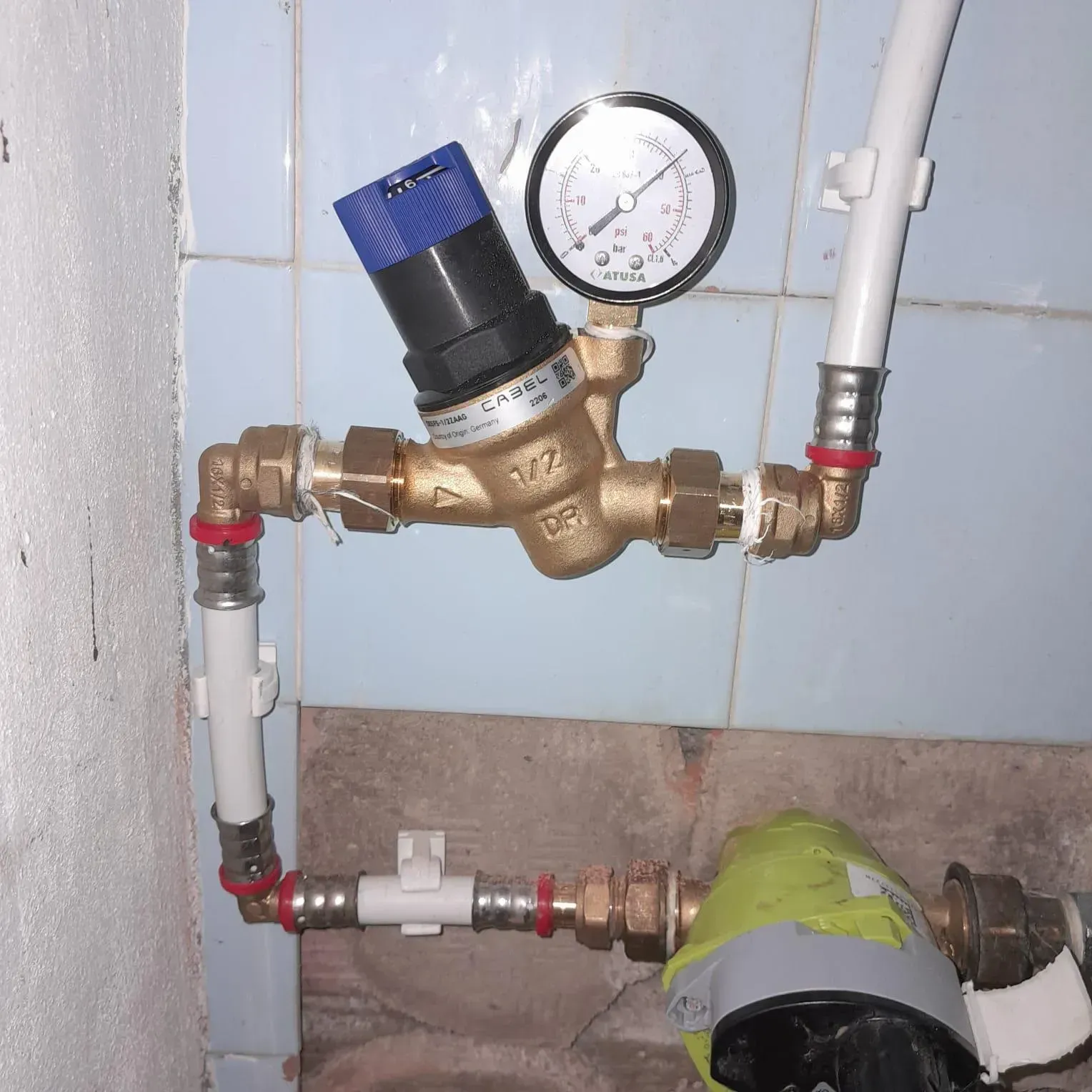 Fontanero instalando tuberías de agua, con guantes rojos, cerca de una válvula y tuberías de cobre.