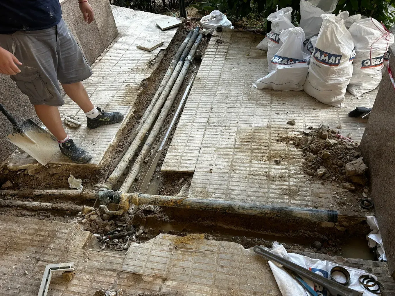Obrero de la construcción excavando una zanja para acceder a unas tuberías instaladas en un patio de ladrillo