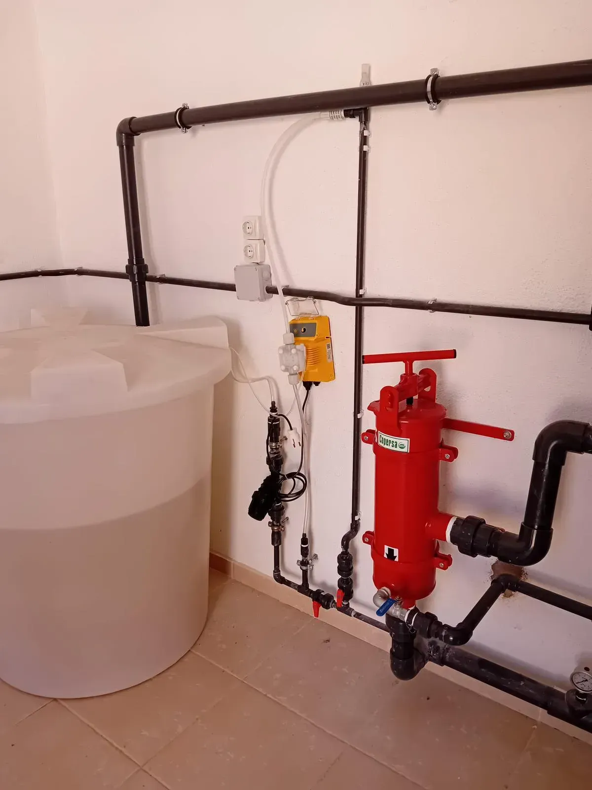 Sistema de tratamiento de agua con tanque blanco, tuberías negras y filtro rojo.