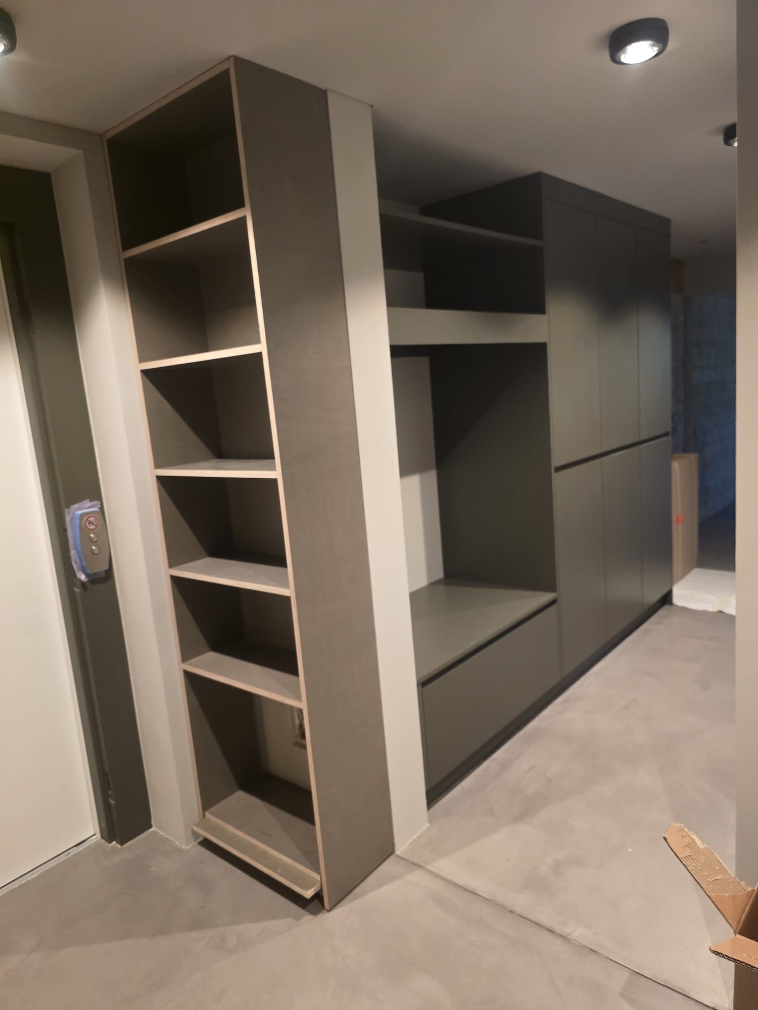 Moderne Küche im Bau mit einer zentralen grauen Kochinsel, Holzschränken und eingelassener Deckenbeleuchtung.