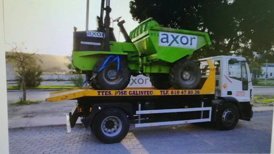 Una cosechadora Green Axor, cargada en un camión de plataforma, estaba estacionada al aire libre cerca de árboles