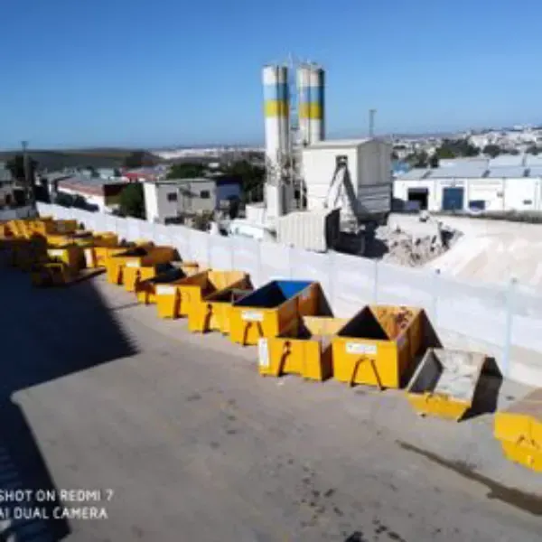 Azotea industrial con contenedores amarillos, edificios blancos y altos silos bajo un cielo azul.