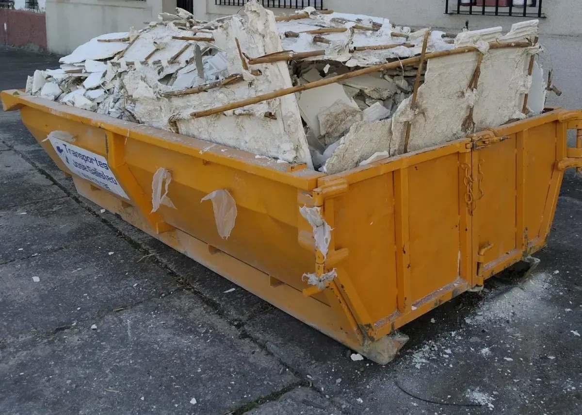 Contenedor de basura naranja lleno de yeso blanco roto y escombros sobre una superficie de hormigón.