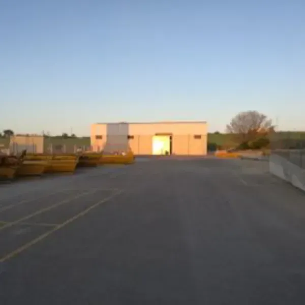 Terreno pavimentado vacío que conduce a un pequeño edificio beige al atardecer.