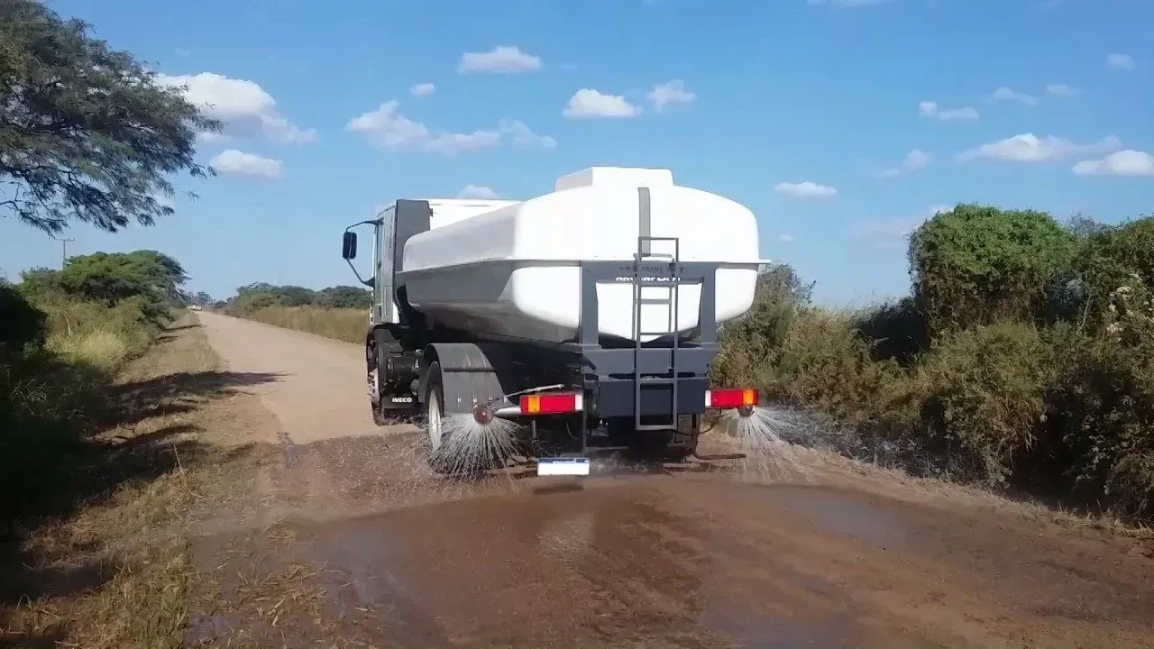 Un camión cisterna blanco circula por un camino rural embarrado, salpicando agua.