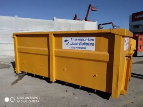 Contenedor industrial amarillo con un letrero de Transportes José Gallego, ubicado al aire libre en un terreno soleado.