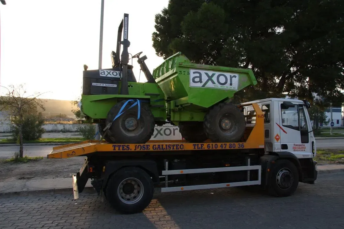 Un rodillo compactador Green Axor cargado en un camión de plataforma al atardecer, cerca de la carretera.