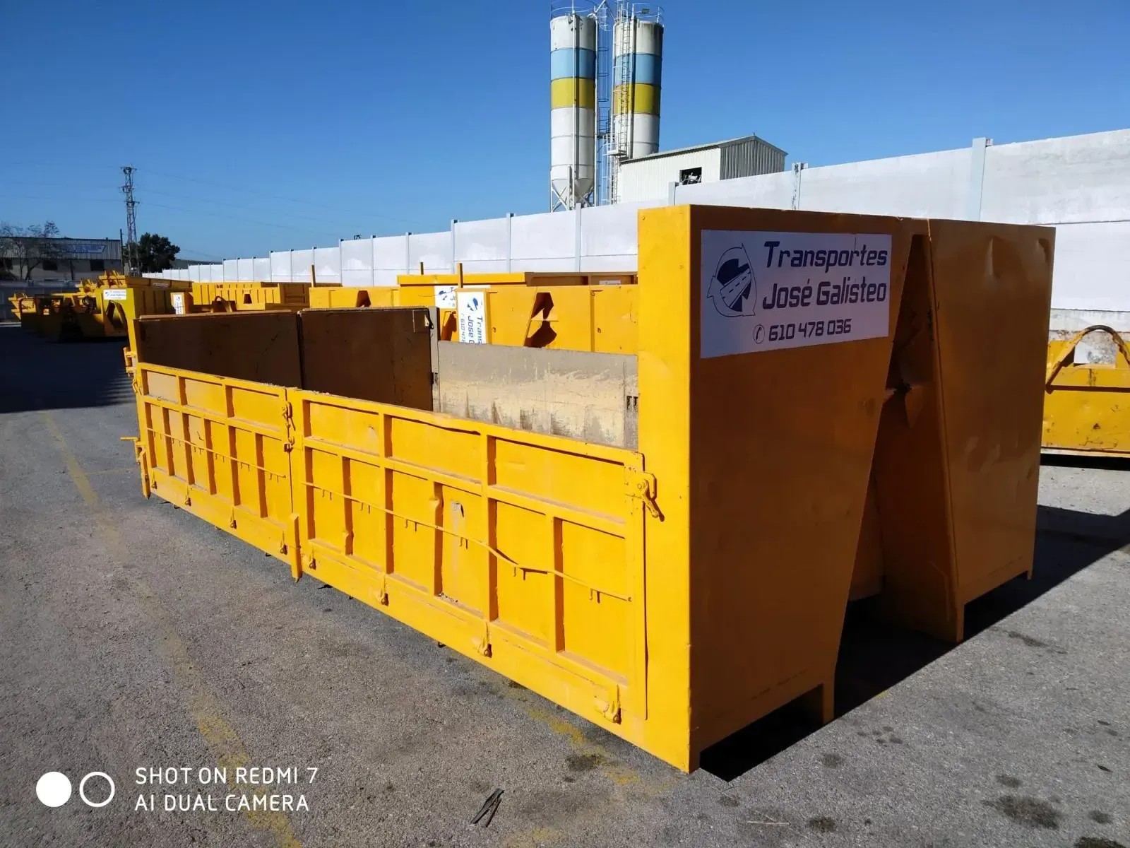Un contenedor industrial metálico amarillo, o basurero, está estacionado al aire libre en un terreno pavimentado