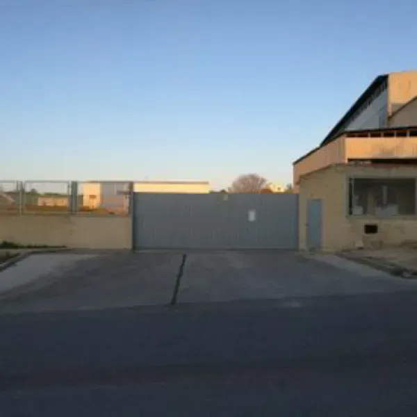 Puerta industrial y edificio junto a un solar pavimentado vacío al atardecer.